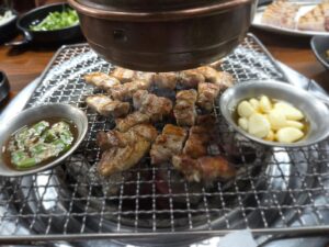 숯불 석쇠에서 한입 크기로 잘라 익히는 삼겹살과 통마늘